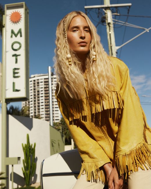 Person wearing a yellow fringed jacket in front of a Motel sign.