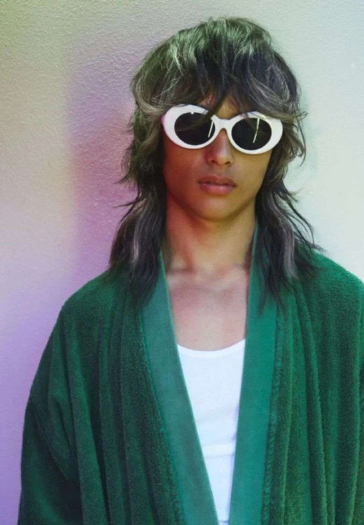 Person wearing a green robe and white sunglasses with a blurred background