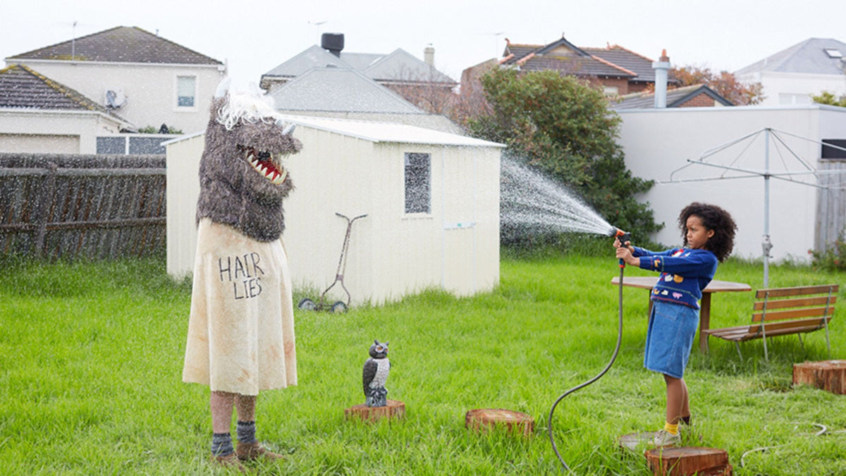 Person in a costume being sprayed with water from a hose by a child in a backyard