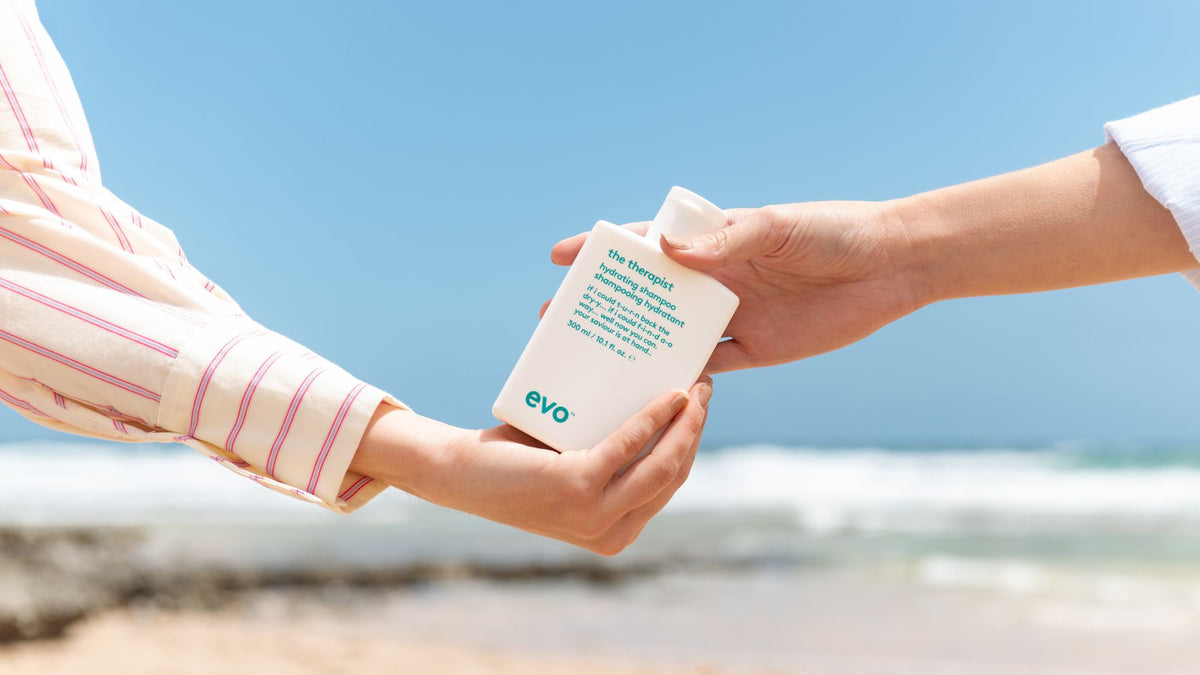 Two hands exchanging a white container with 'evo' branding against a clear blue sky.