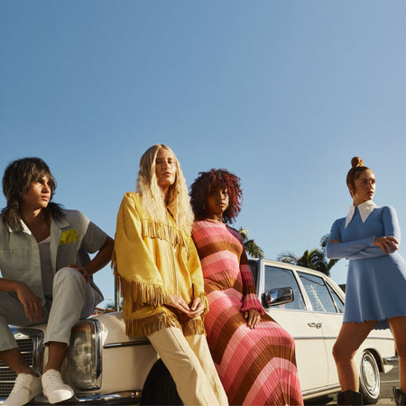 Three women and a man sitting on a classic car against a clear blue sky