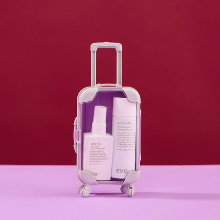 Small suitcase with evo hair products on a pink and red background