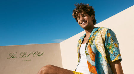 Man in colorful shirt sitting on a wall with 'The Pool Club' sign in the background